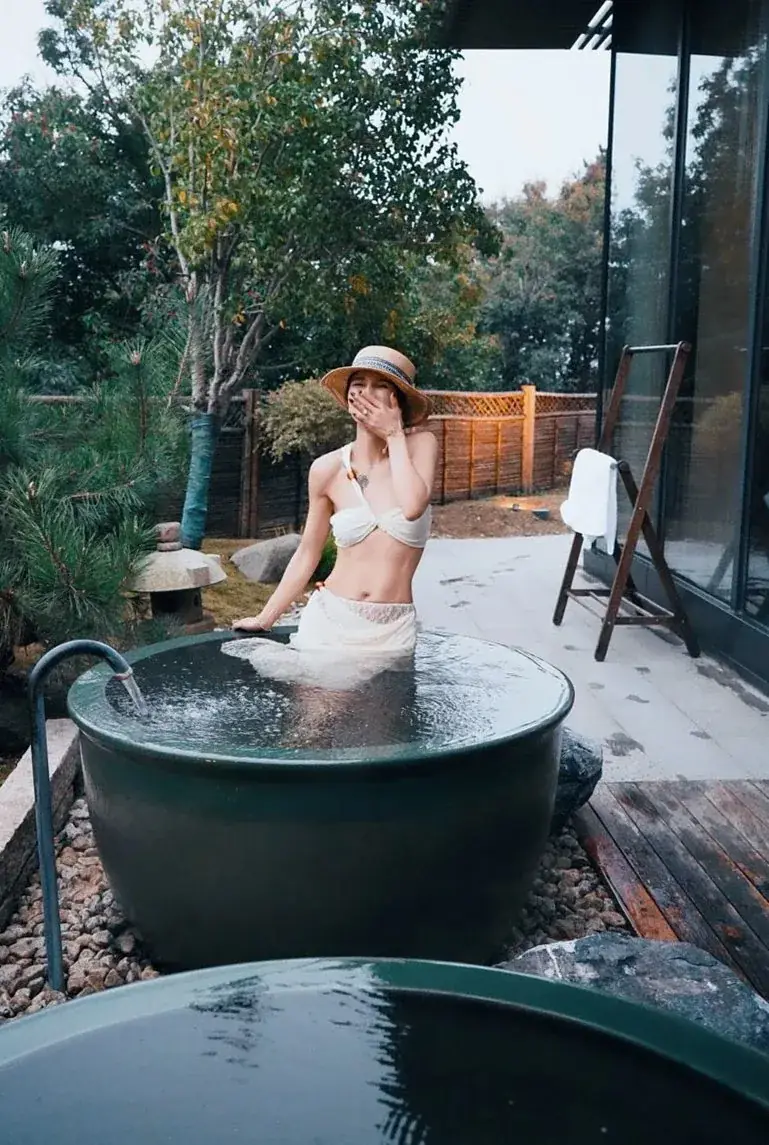 Person relaxing in a round black tub on a wooden deck